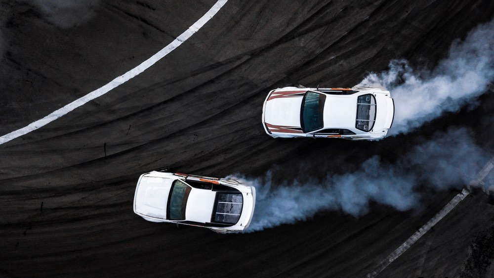 Two cars drifting around a tight bend. High-speed shot on a race track. Drone photography from a bird's eye perspective.