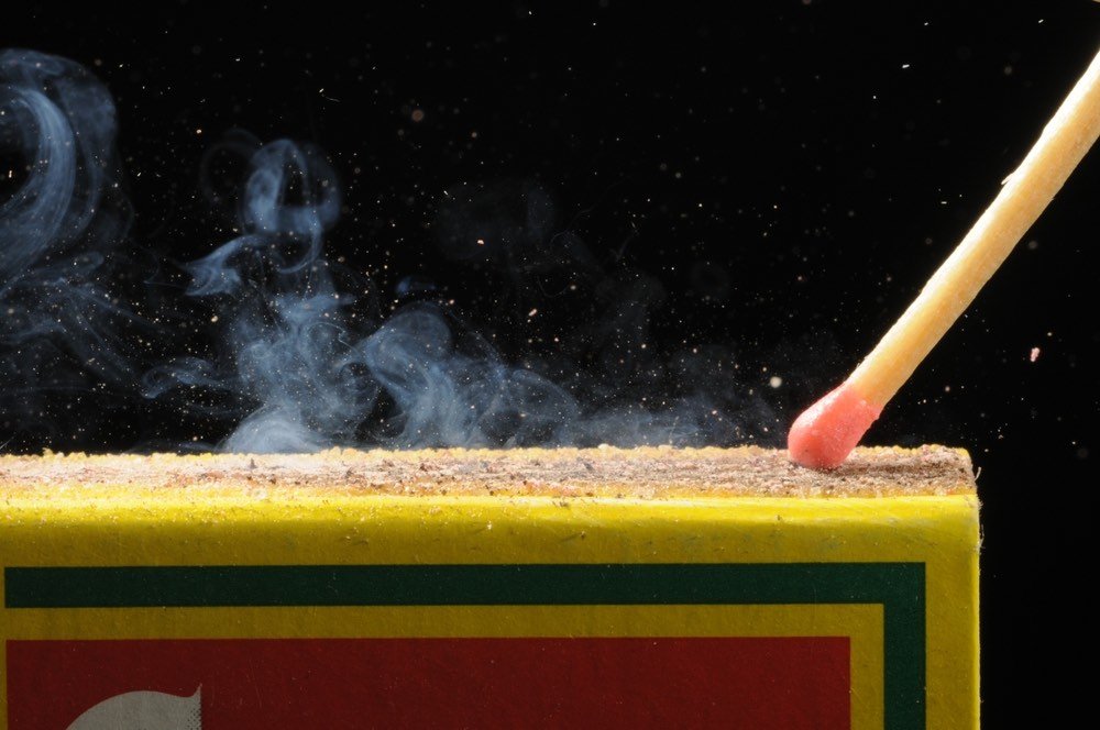 High-speed Closeup of matchstick burning. Small tufts of smoke against black background.