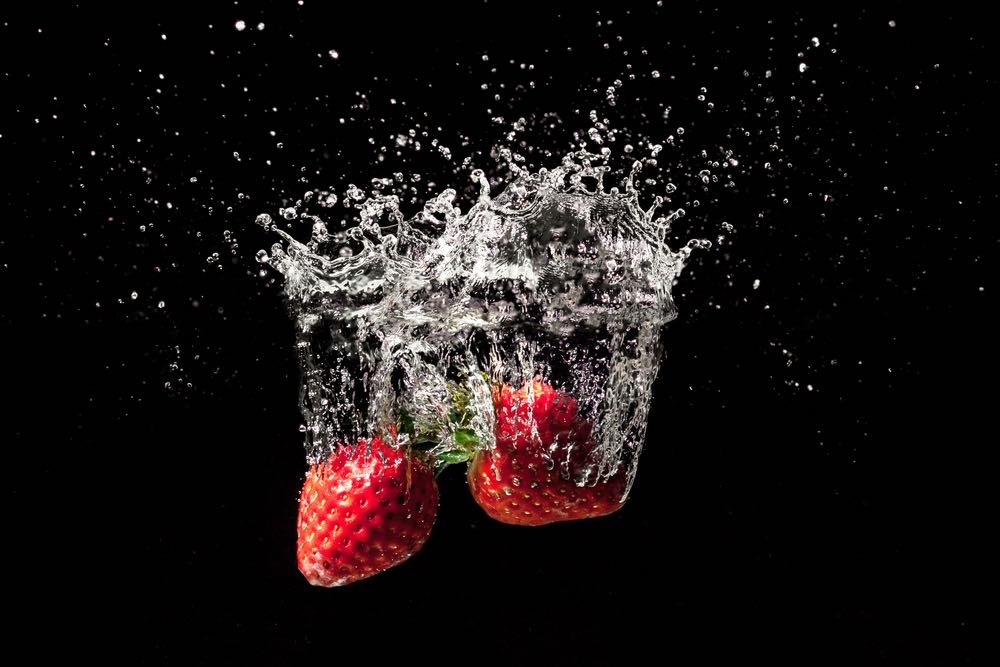 Strawberries sinking into water. High-speed image of water droplets splashing on impact. Dark background.