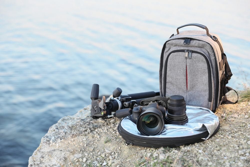 An assortment of camera gear next to a suitable backpack for carrying. Tripod, camera, lenses, and more.