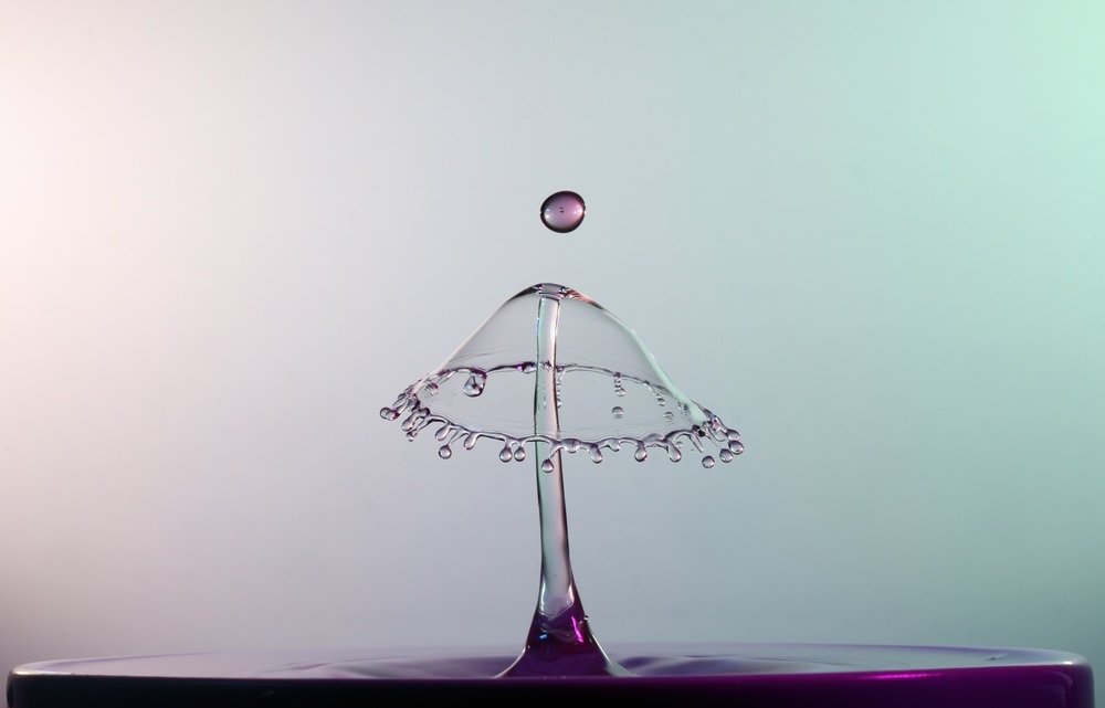 Close-up, high-speed photo of water droplet landing in a puddle. High-detail shot of water drops flying against a clear backdrop.