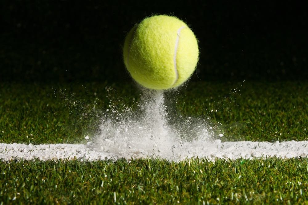 Close-up view of a tennis ball landing on court. High-resolution shot of impact, with chalk visible in the air trailing the ball in high detail.